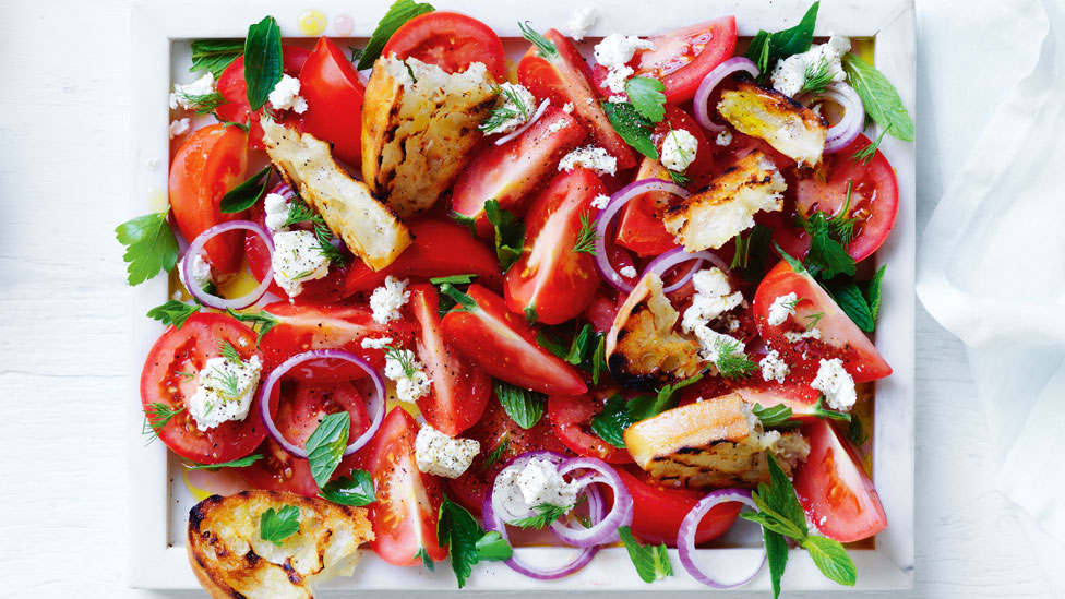 Fresh tomato and bread salad with fetta, garnished with parsley, mint and dill prigs.