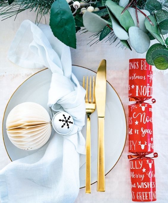 A christmas plate set up with a cracker, a tied cloth and gold cutlery