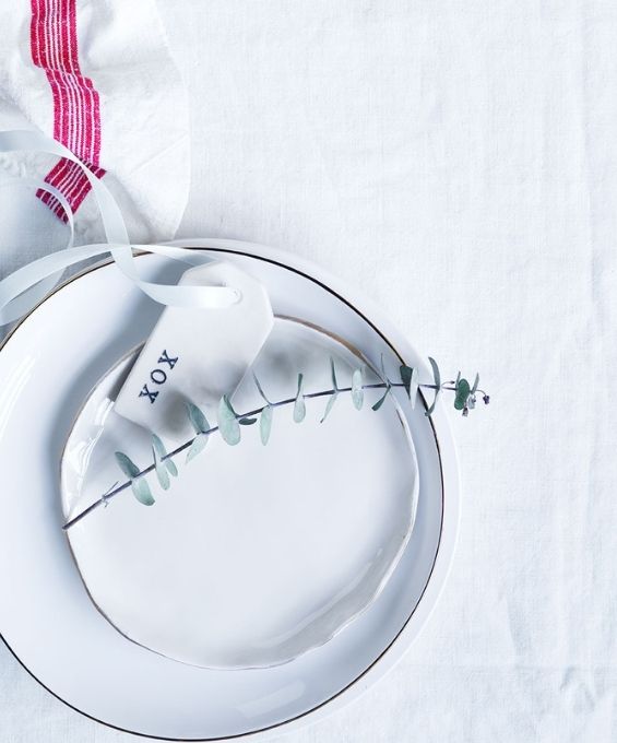 A table cloth drapped across a white table with two white plates with a stem of dried leaves