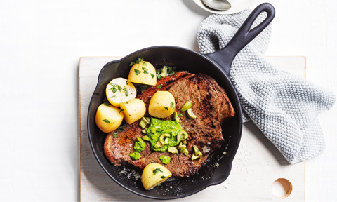 Pesto and olive steak served with potatoes in an iron skillet 