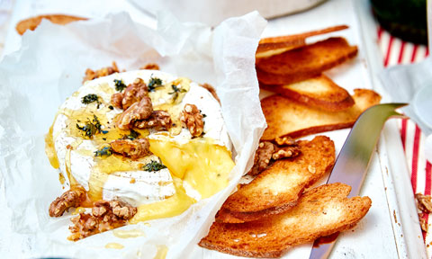 A baked brie cheese with thyme and walnuts on top, served with crispy bread