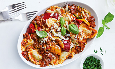 Spinach and ricotta agnolotti with zucchini and bolognese sauce, garnished with basil leaves.