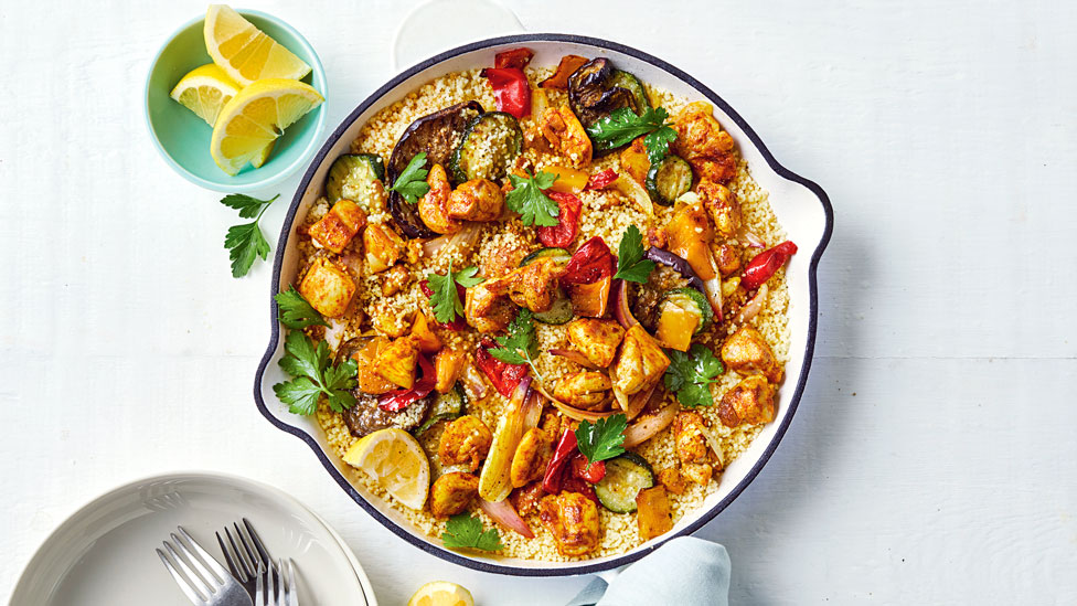 A bowl of chicken paella topped with herbs and a side of lemon