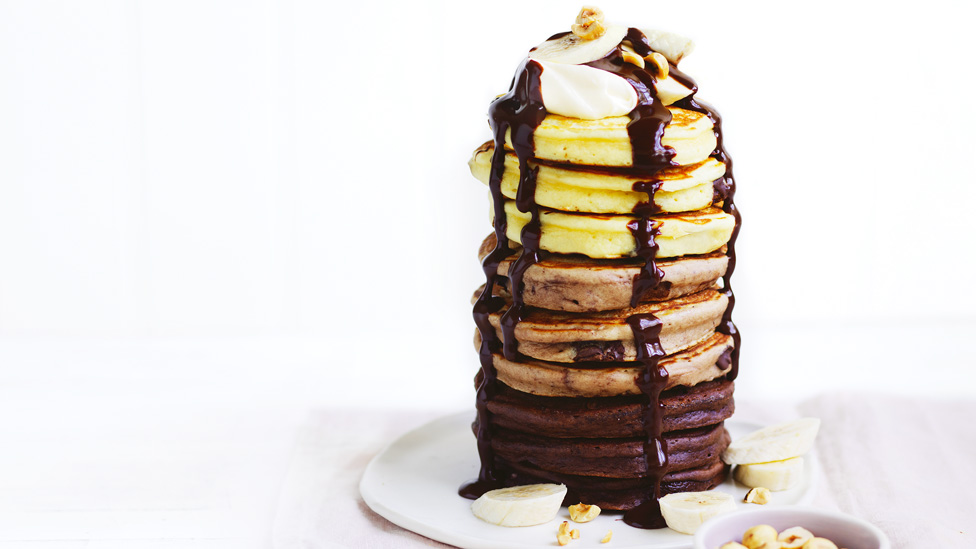 Tri coloured pancakes topped with chocolate sauce, banana, cream and hazelnuts