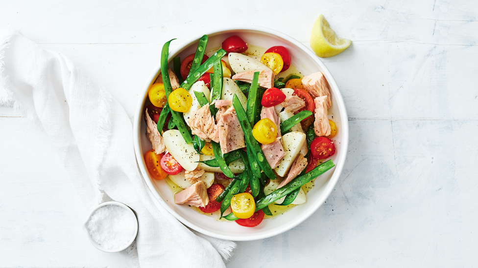 A bowl of tuna salad with beans, tomatoes and lemon