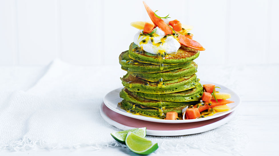A stack of green pancakes topped with mango, papaya, and passionfruit