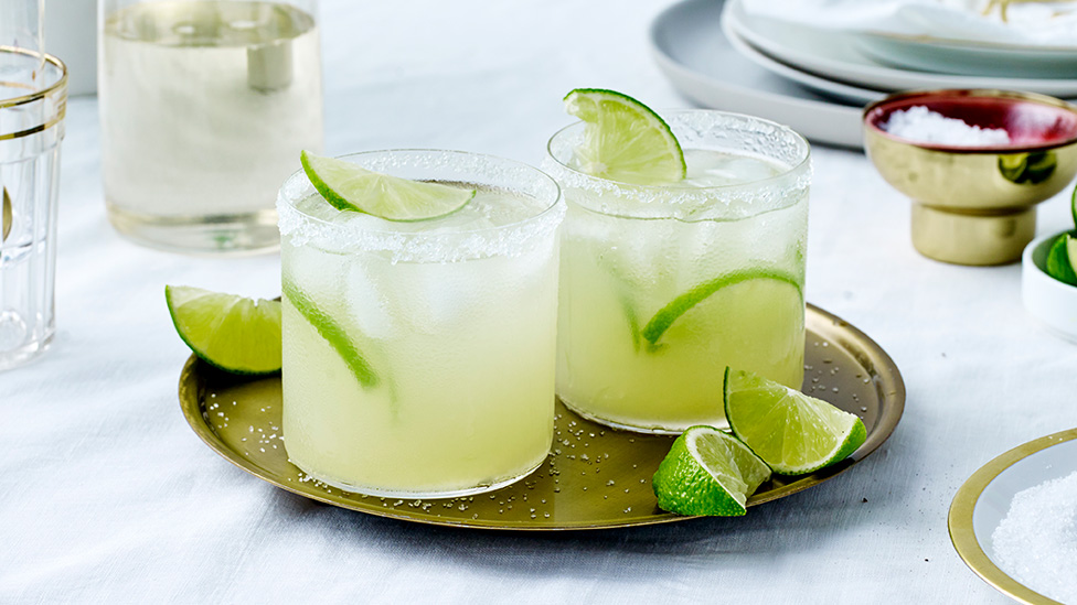 2 glasses of margarita garnished with limes
