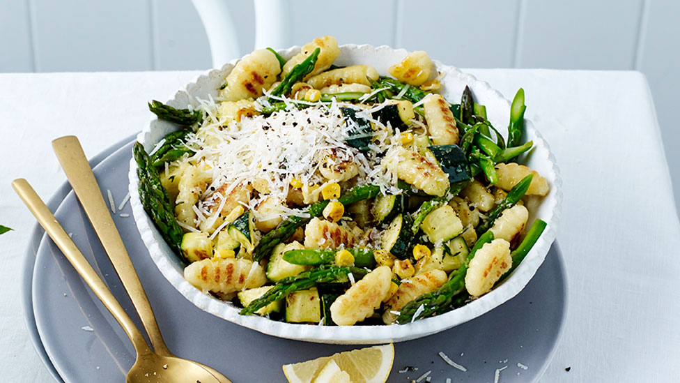 A bowl of pan-fried potato gnocchi with summer vegetables topped with cheese