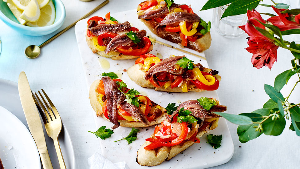 Slices of toasted bread topped with roasted capsicum and anchovy fillets