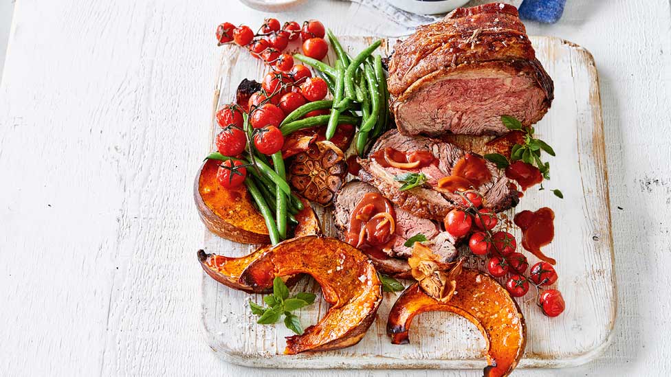  Roast Beef with Tomato and Red Wine Gravy on a wooden board. Served with tomato on the vine and pumpkin.