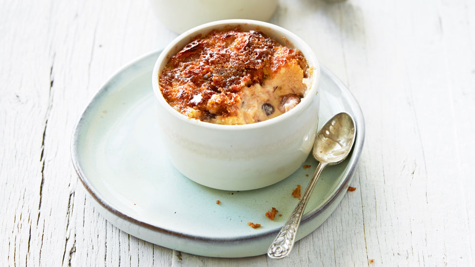 A ramekin containing hot cross bun creme brulee on a plate with a spoon alongside