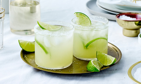 2 glasses of margarita garnished with limes