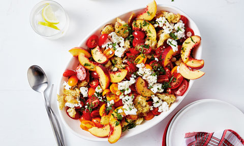 A bowl of perino and peach panzanella salad topped with herbs