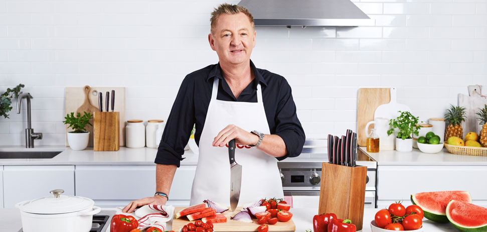 Luke Mangan standing at kitchen bench holding a knife