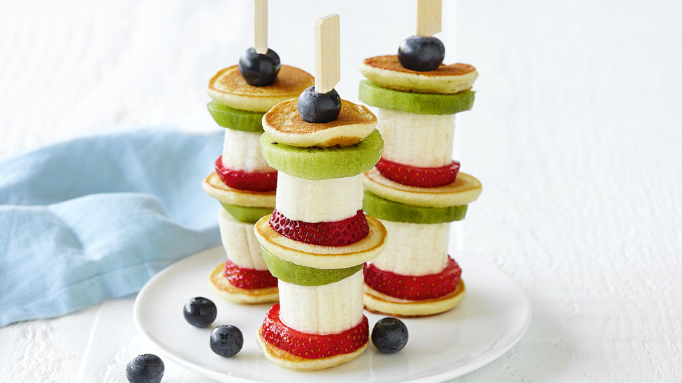 Three mini banana pancake stacks with kiwifruit, strawberry and blueberries