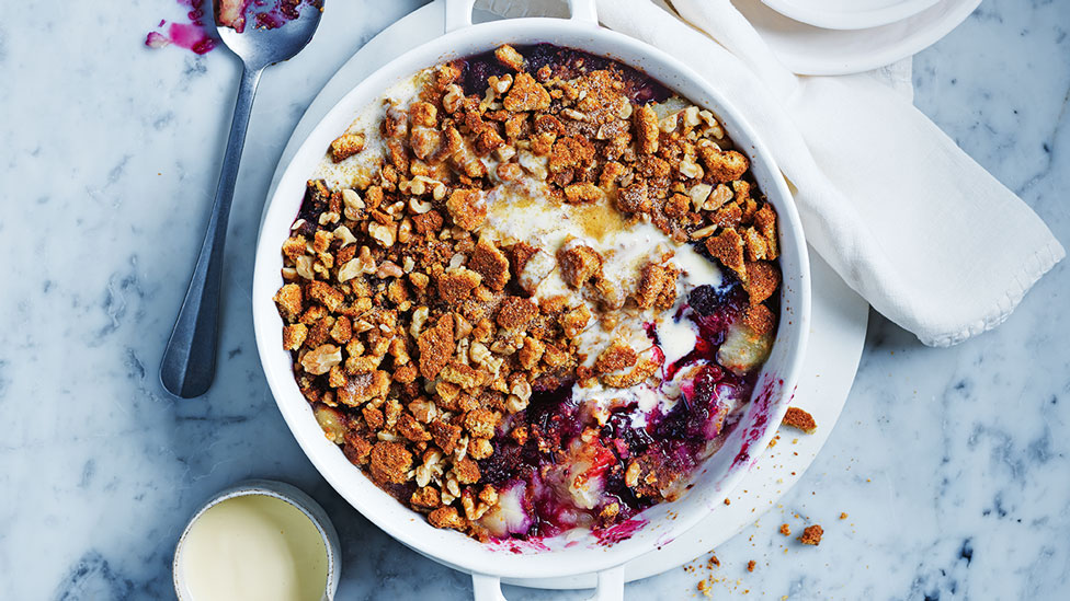 Apple berry crumble served in a bowl with crumbled gingernut biscuits and walnuts on top