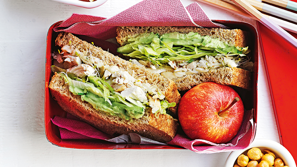 Green goodness sandwich cut in half and served in a lunch box with an apple