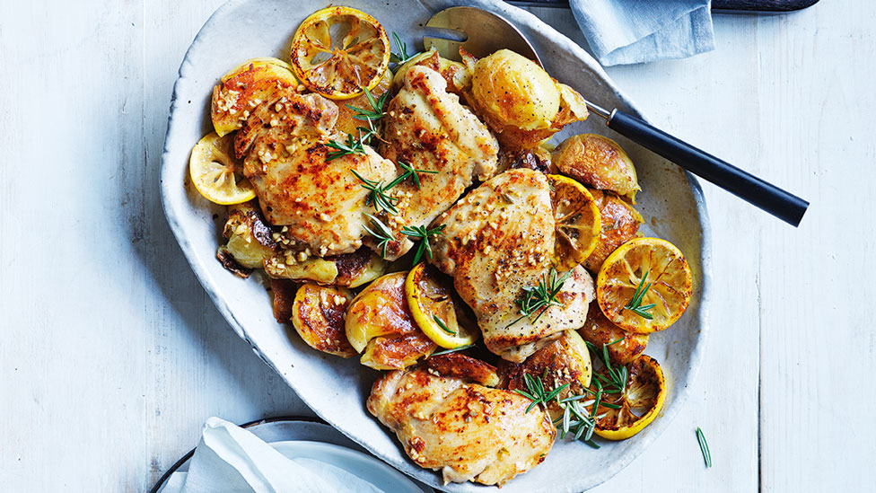 Baked lemon rosemary chicken served on a serving platter with grilled lemon and herbs