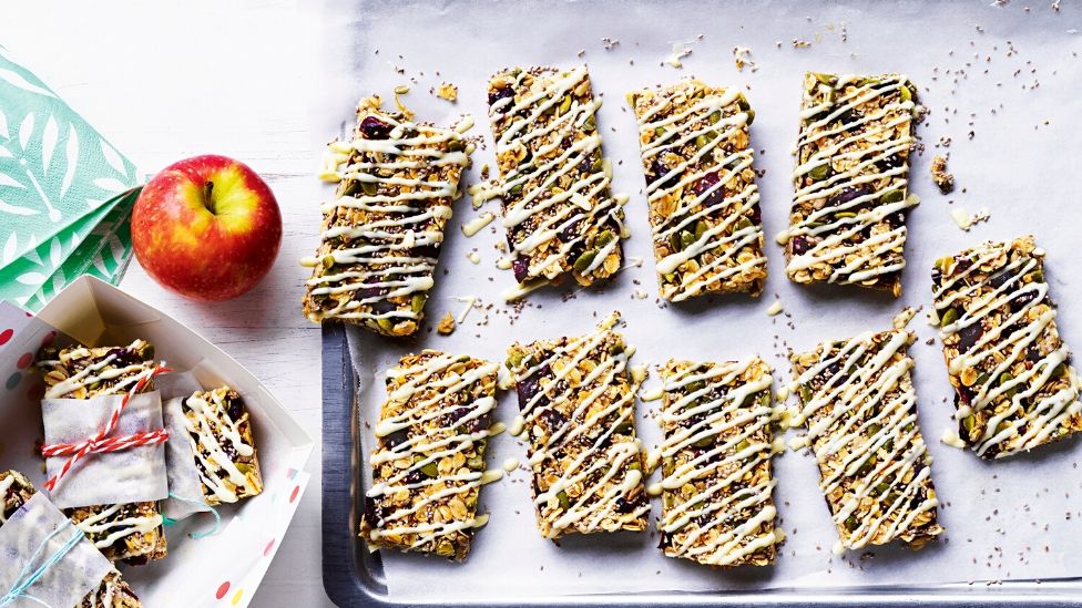 Muesli bars arranged on a tray with yoghurt drizzle and an apple on the side