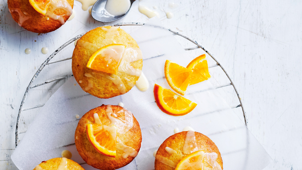 Five orange muffins with icing and sliced orange on top