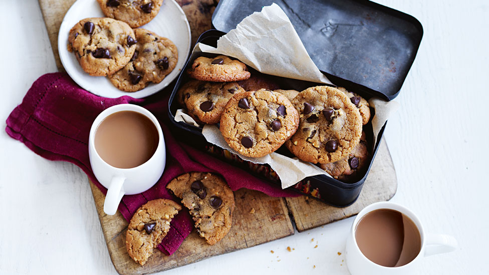 Peanut butter and choc chip cookies served in a baking tin with a cup of tea beside