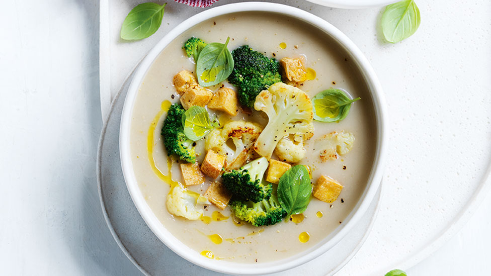Cauliflower and broccoli soup served in a bowl with croutons and basil
