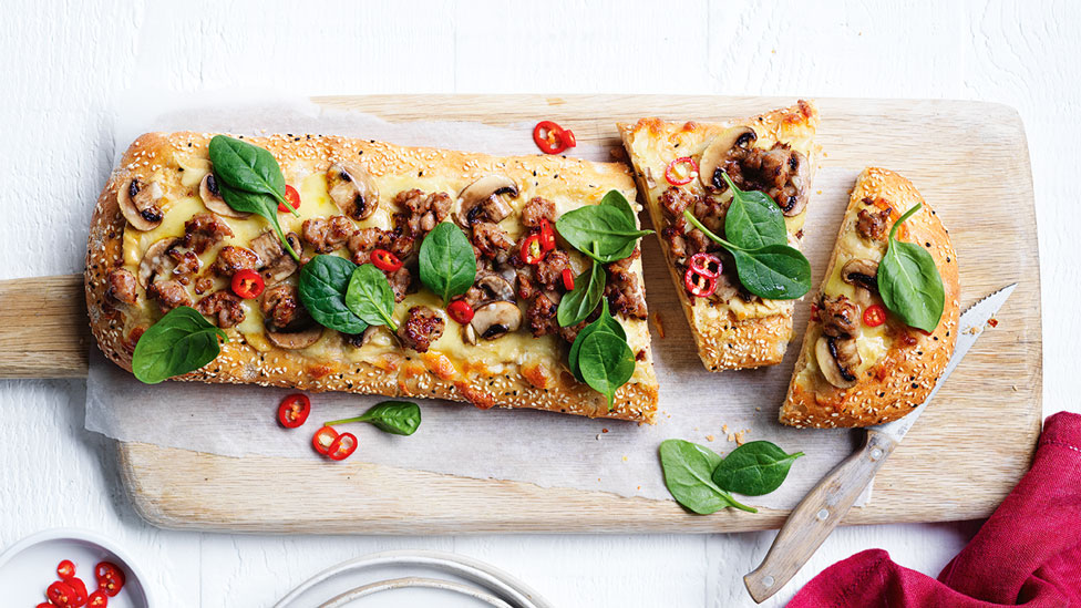 Sausage and mushroom pide served on a chopping board and cut into three sections