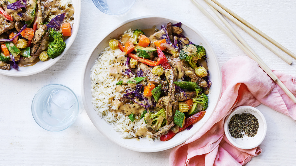 Beef stir fry served in a bowl with rice and vegetables with black poppy seeds on the side