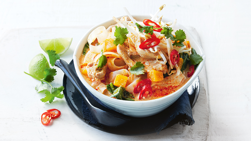 Chicken laksa in a bowl with bean sprouts, chilli and coriander with lime wedges on the side