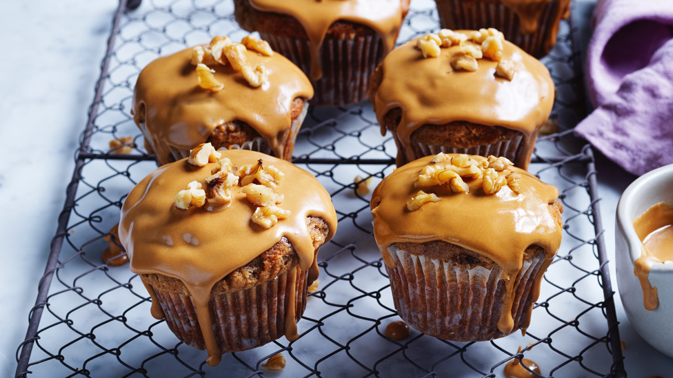 Four muffins arranged on a cooling tray with coffee glaze and walnuts on top