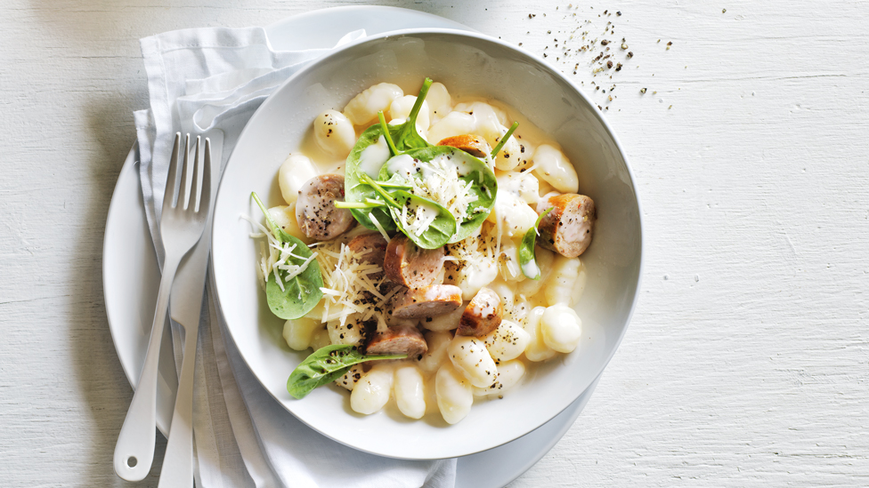 Gnocchi served in a bowl with spinach, sausage and parmesan cheese on top