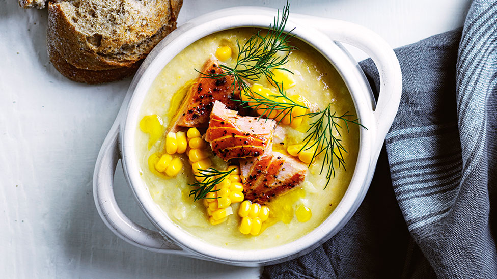 Bowl of corn, cauliflower and coconut chowder topped with salmon portions and dill