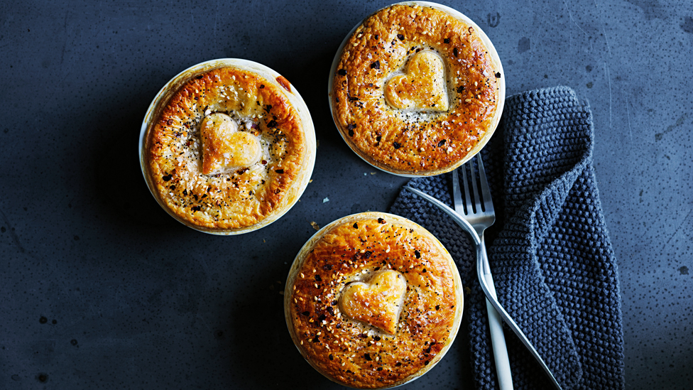Three chicken pies on a benchtop with a knife and fork