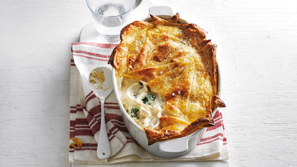 Whole chicken and mushroom pie served in a baking dish on top of a tea towl and serving spoon