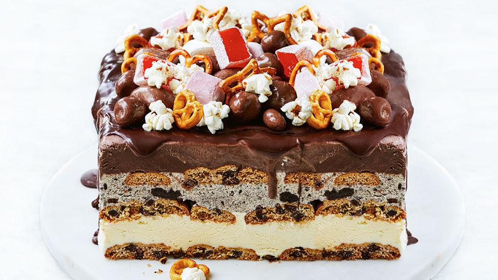 Ice-cream cake on a cake stand topped with popcorn, pretzels and turkish delight