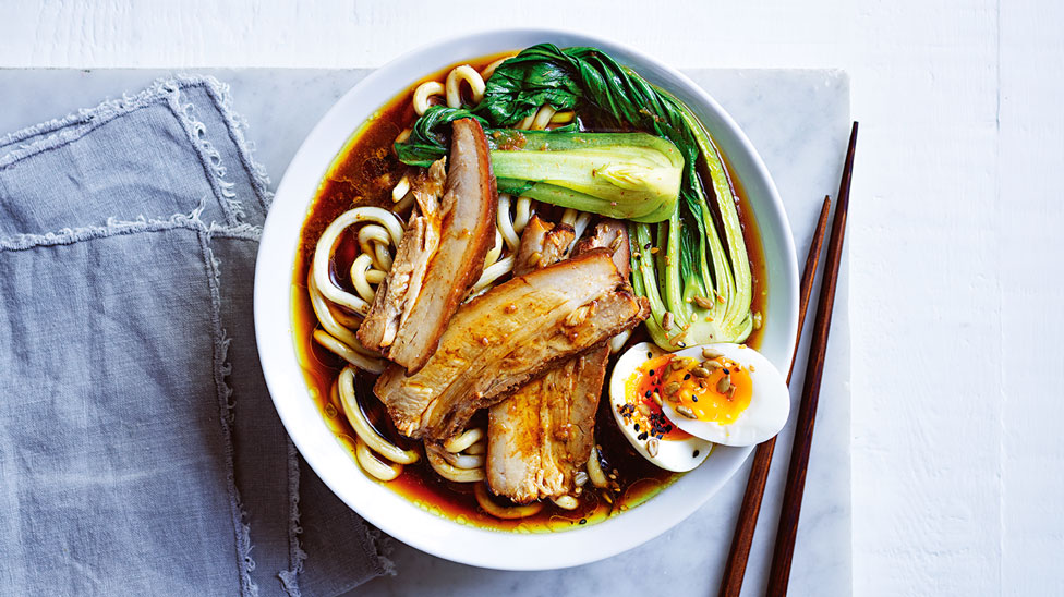 Japanese soup with noodles, pork, egg and bok choy served in a bowl with chop sticks