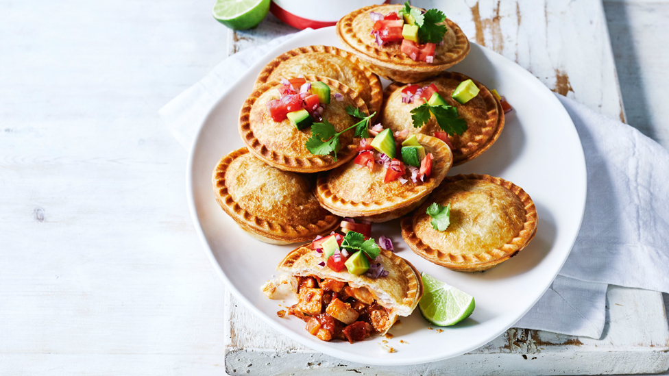 Mexican chicken pies stacked on a plate with avocado on top and lime wedge on the side