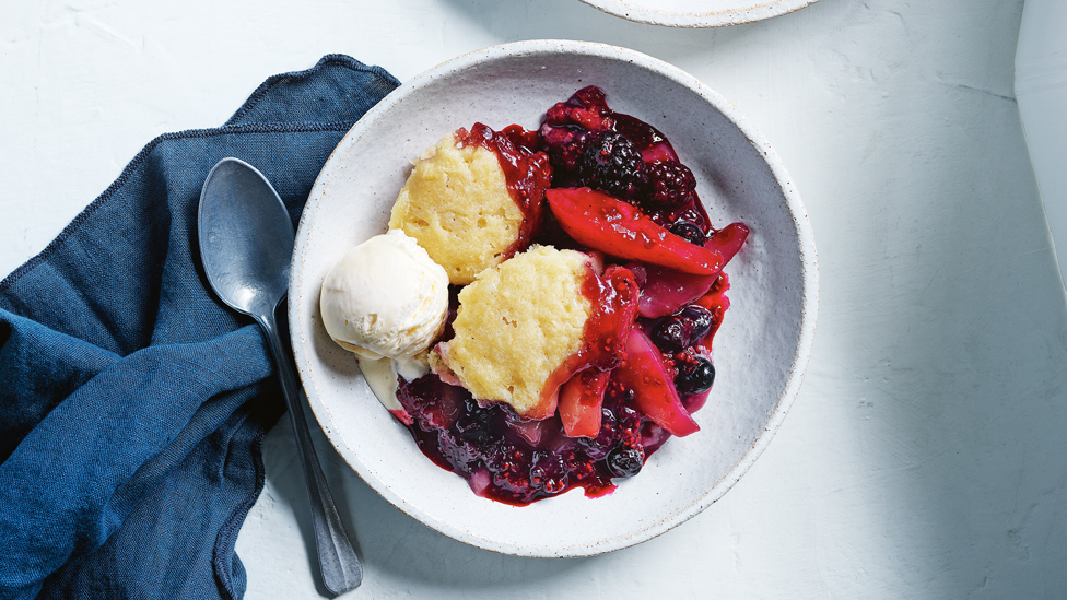 Pear, berry and white chocolate cobbler served in a bowl with a scoop of ice-cream on the top