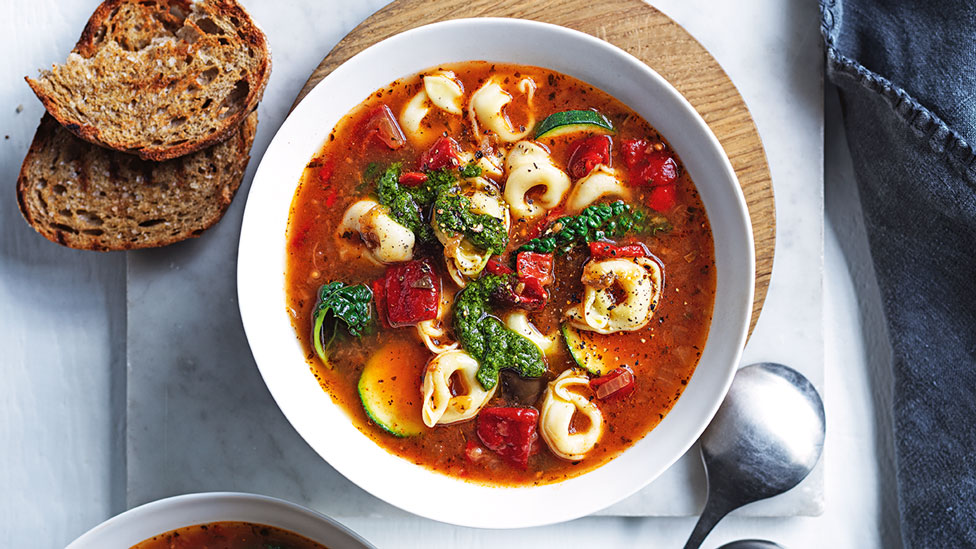 A bowl of ratatouille soup with cheese tortellini and bread on the side
