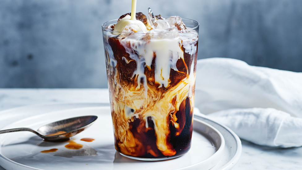 Vietnamese coffee served in a tall glass with a sppon on the side