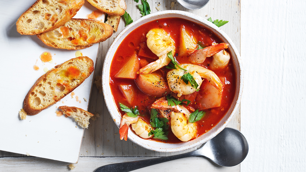 Prawn and potato soup served in a bowl with chilli toast on the side and coriander on top
