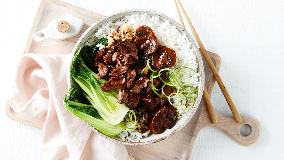 Sticky slow cooked beef served a bowl with rice and bok choy with chop sticks on the side