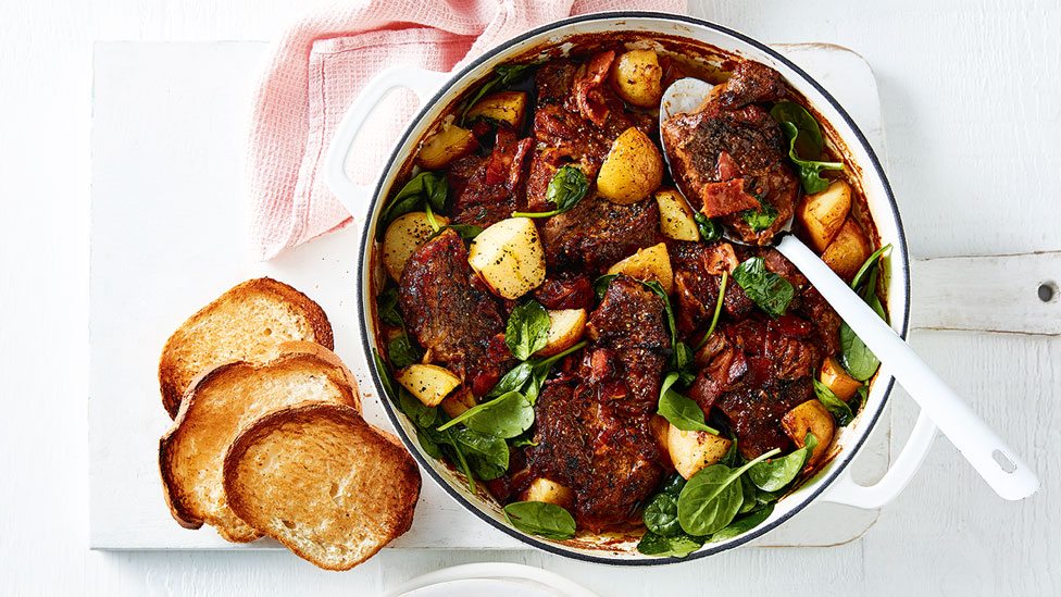 Beef and potatoes served in a bowl with spinach and bread on the side