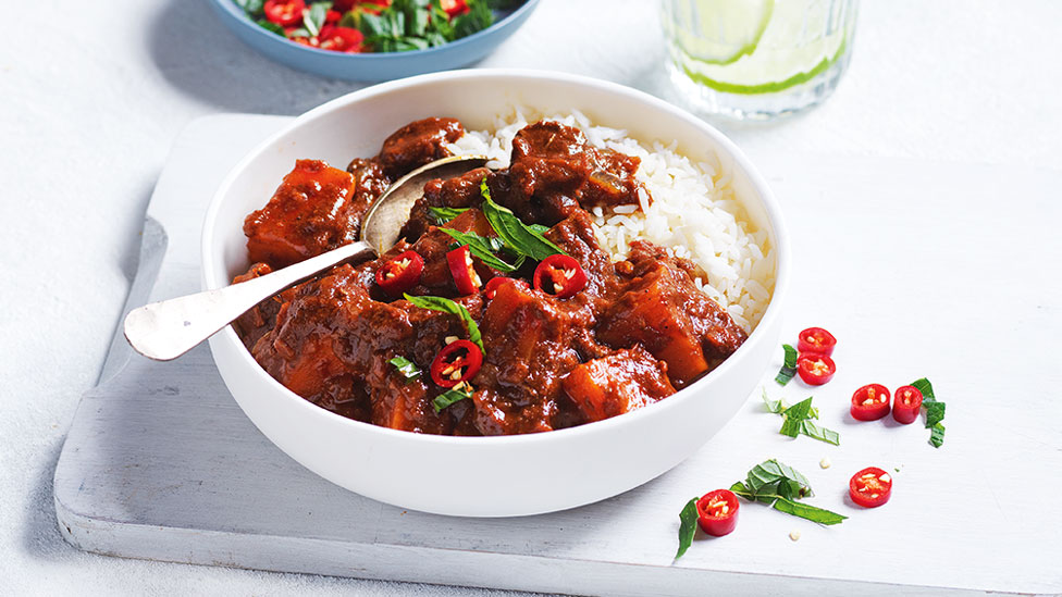 Beef vindaloo served in a bowl with rice and mint and chilli on top