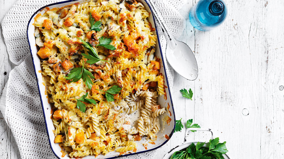 Chicken and mushroom pasta bake in a baking tray with parsley garnish and a serving spoon on the side