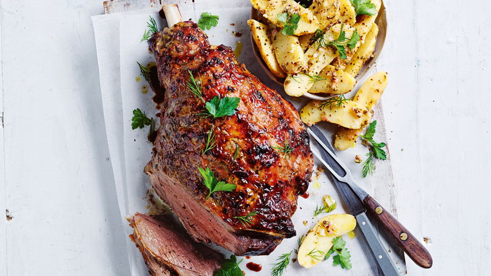 Roast lamb leg served on a dish with potato salad with parsley garnish