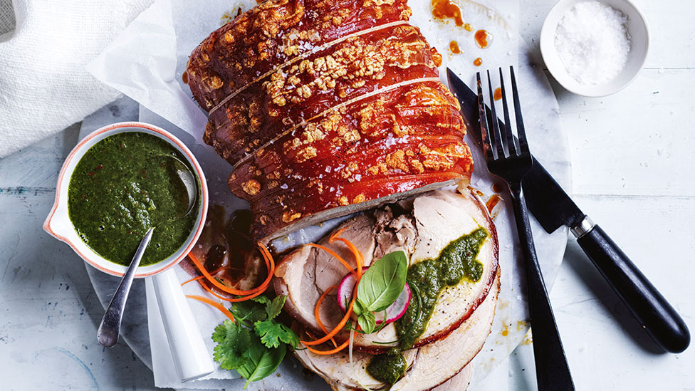 Roast pork served with greens and mustard sauce, knife and fork laid beside pork roast