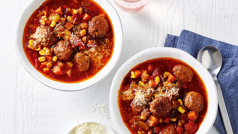 Meatball minestrone served in two bowls with parmesan cheese on the side