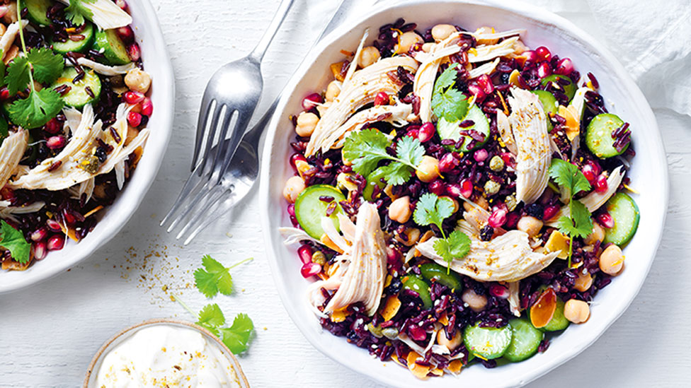 Chicken, cucumber and black rice served in a bowl with corriander garnish with two forks beside the bowl