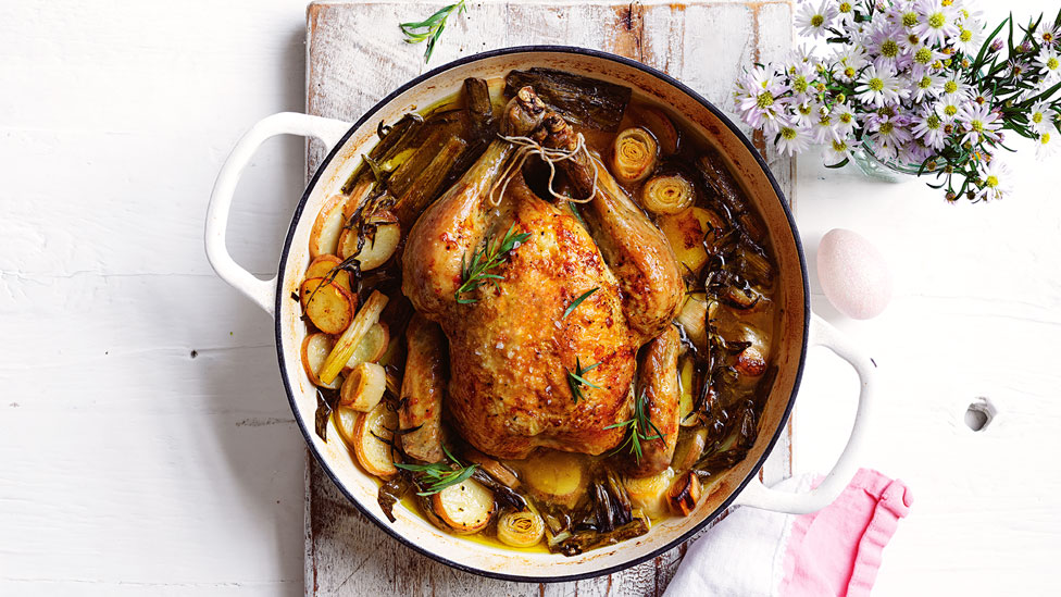 Roast chicken served in a casserole dish with leeks and rosemary sprigs 